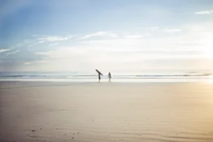 Two surfers walking sandy beach