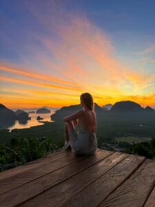 a woman sitting on a wooden deck overlooking a lake and mountains